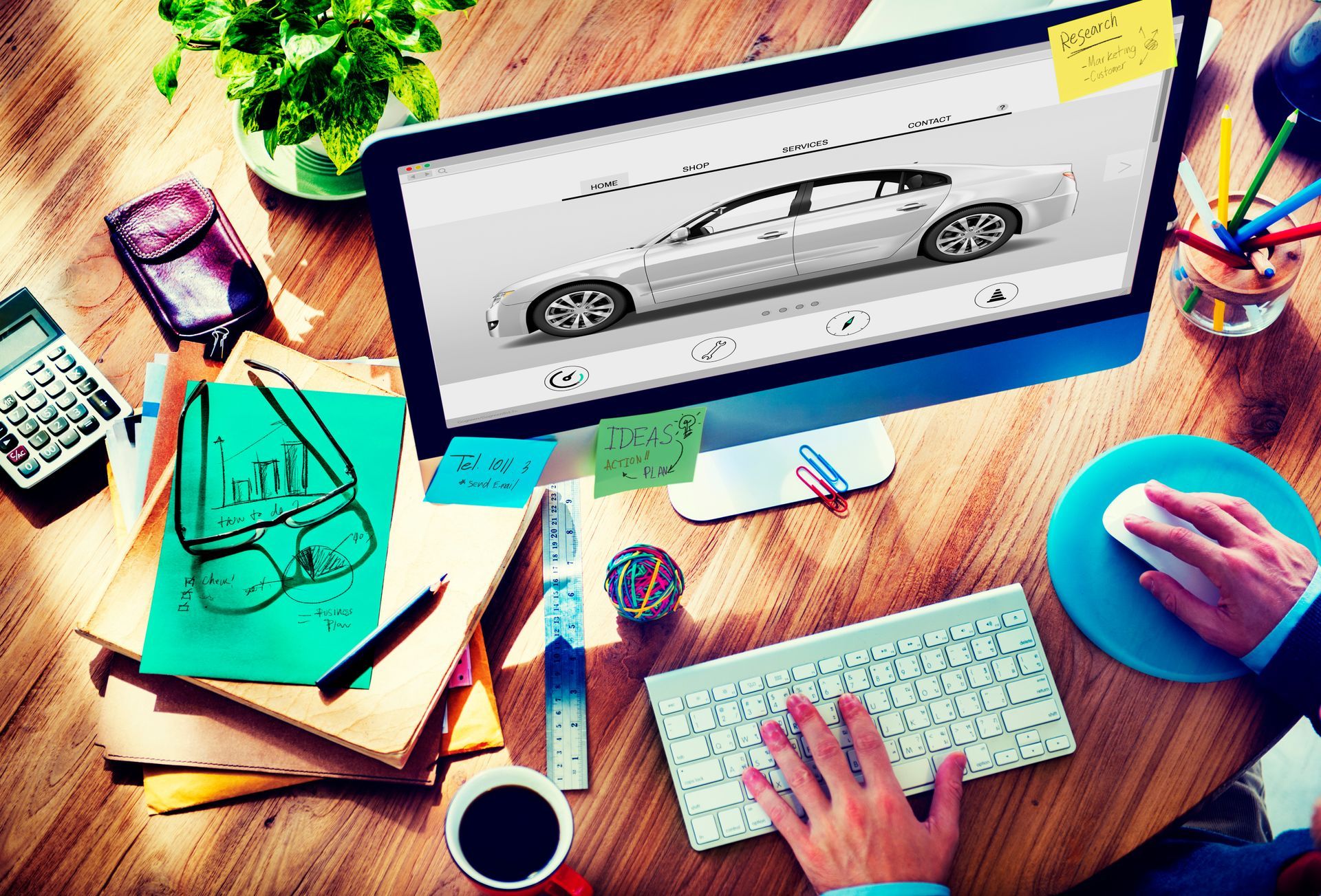 A person is sitting at a desk using a computer with a car on the screen.