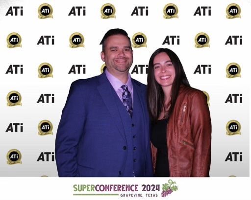 A man and a woman pose in front of a superconference sign