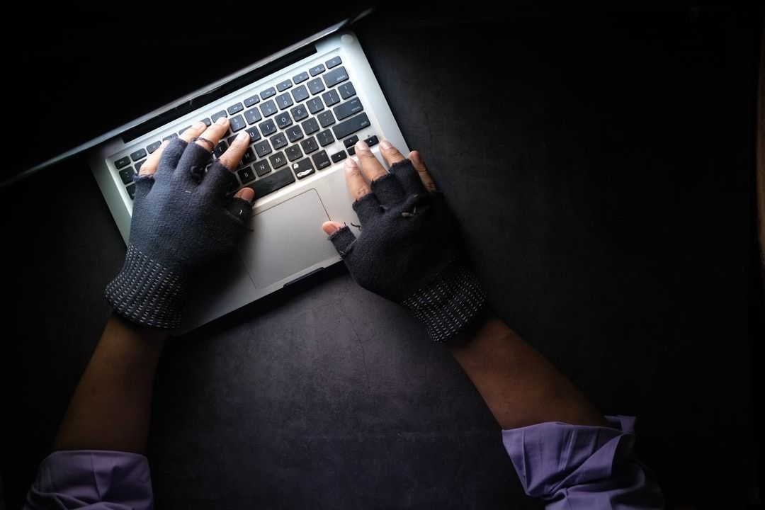 Person in gloves typing on laptop in dark setting, symbolizing Instagram hacked scenario.