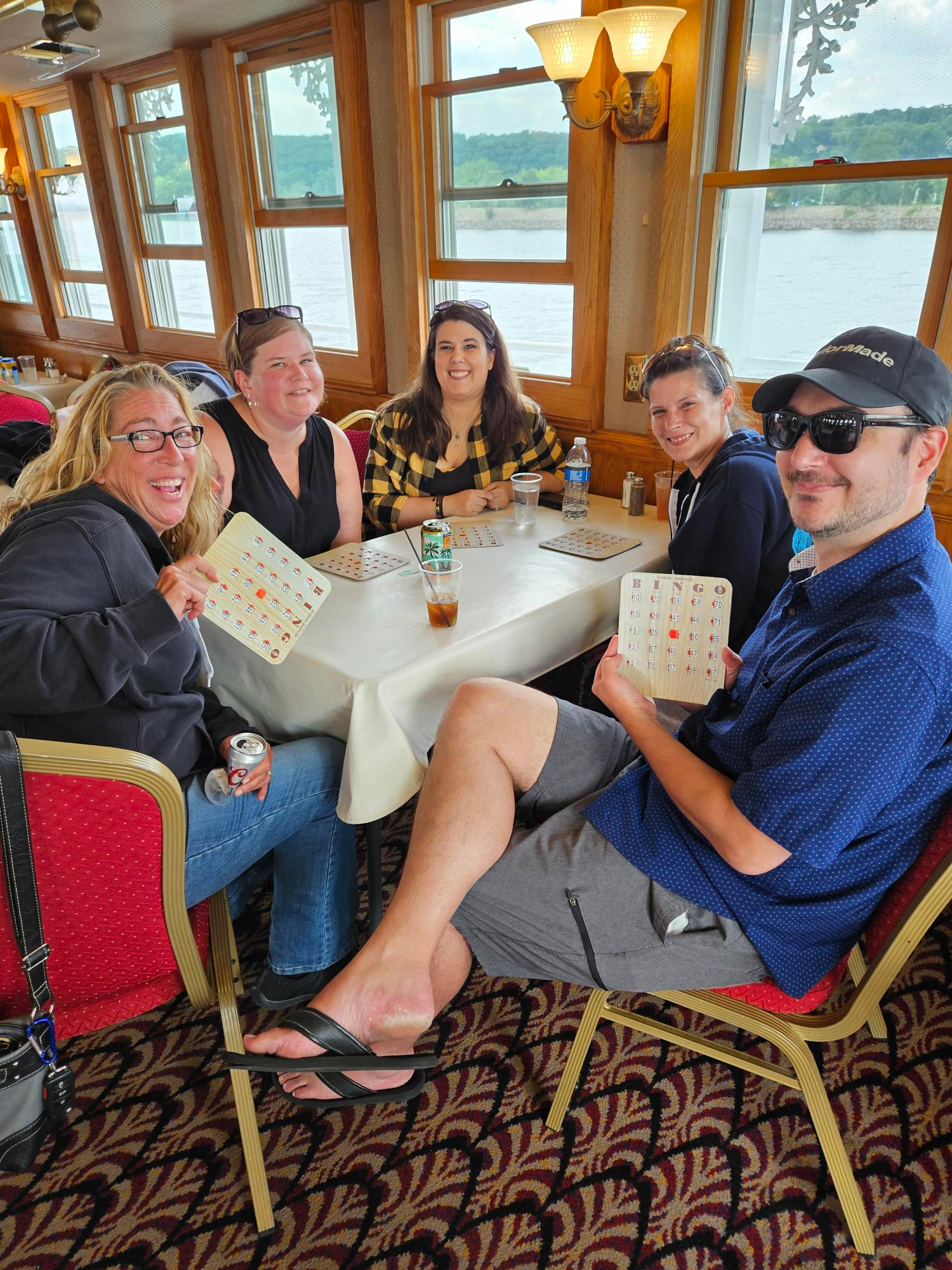 A group of people are sitting around a table on a boat holding bingo cards