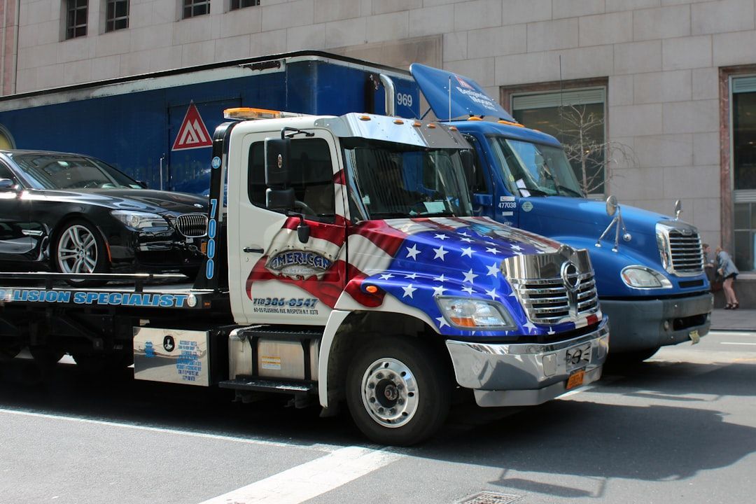 Tow company marketing with a branded American flag tow truck transporting a car in an urban setting.