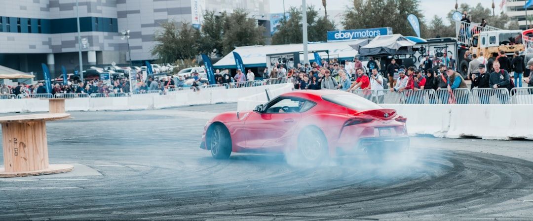 Red sports car drifting at SEMA event surrounded by a crowd and tire smoke