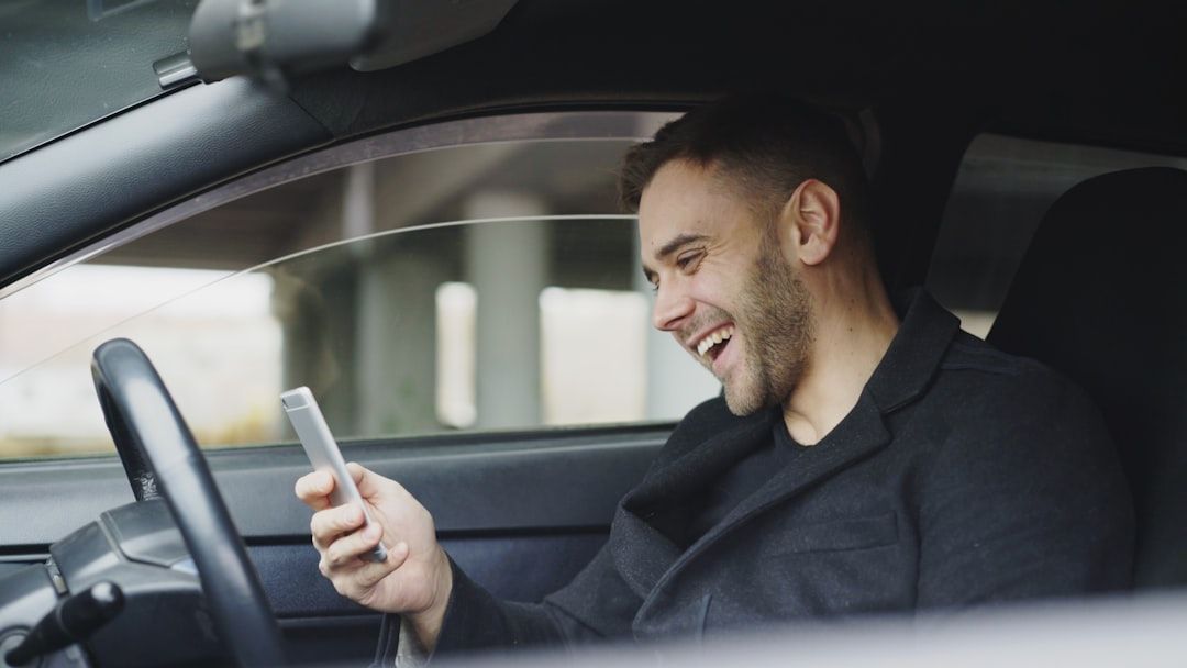 Man in car smiling at phone using SMS marketing.