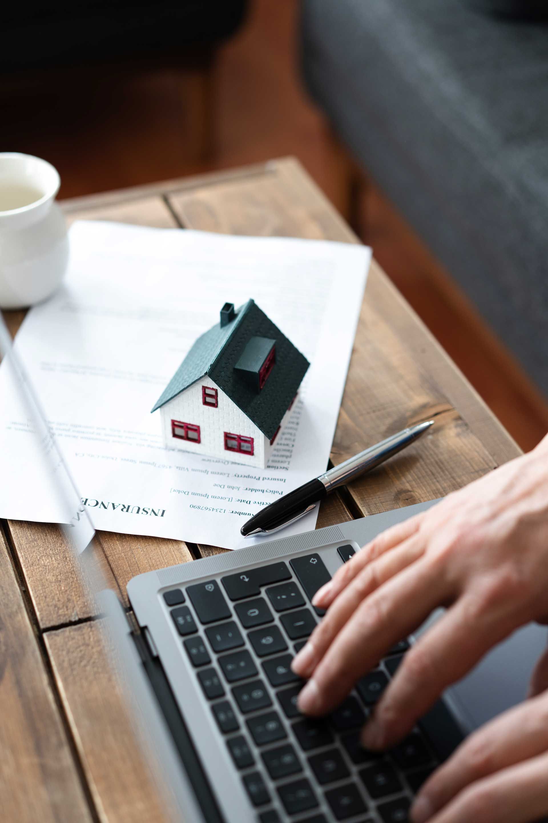 Insurance agency representative works on a laptop with home policy and house model on the desk. Insurance agency representative works on a laptop with home policy and house model on the desk.