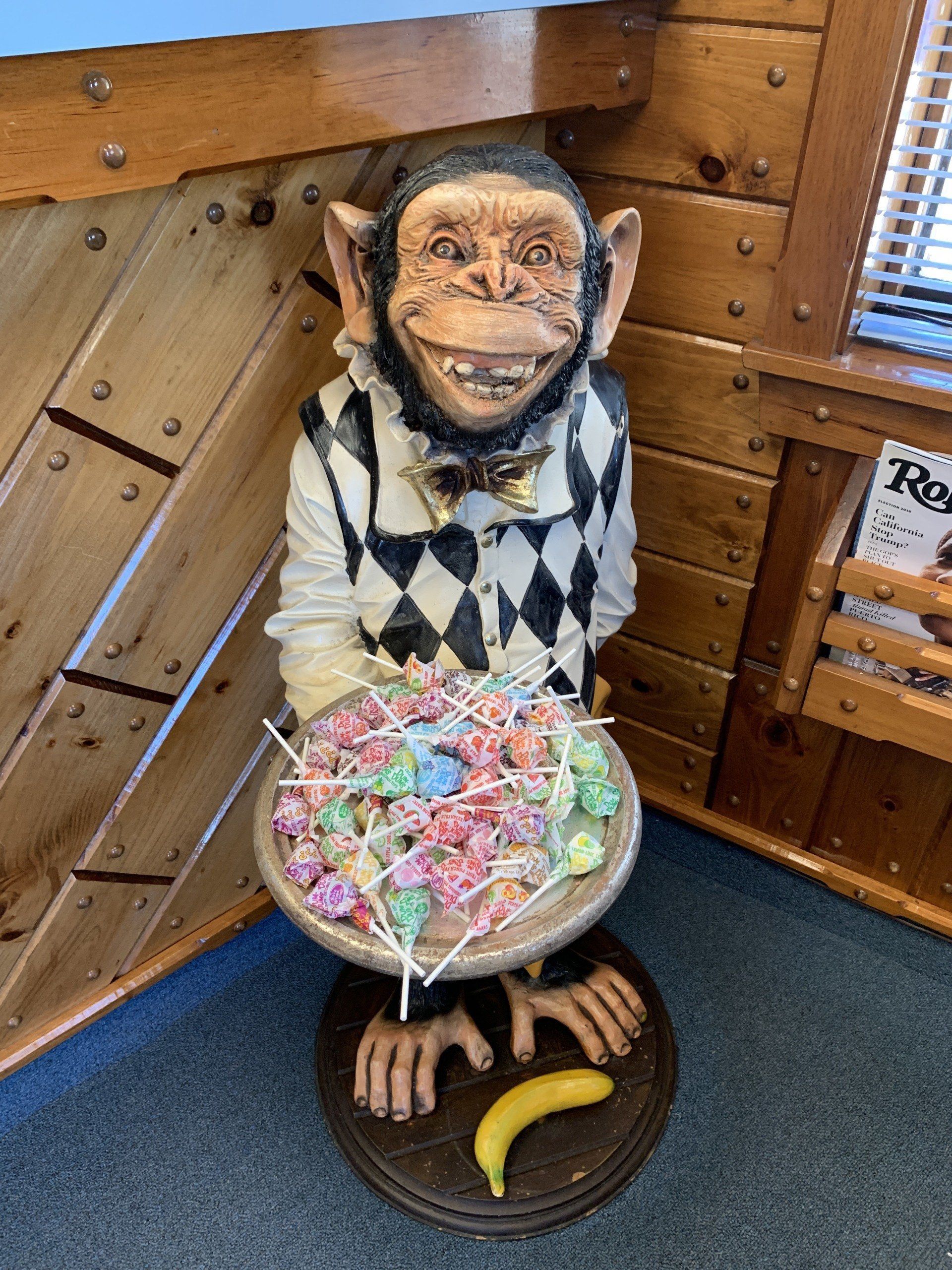 Statue of a monkey holding a bowl of lollipops, with a banana at its feet.
