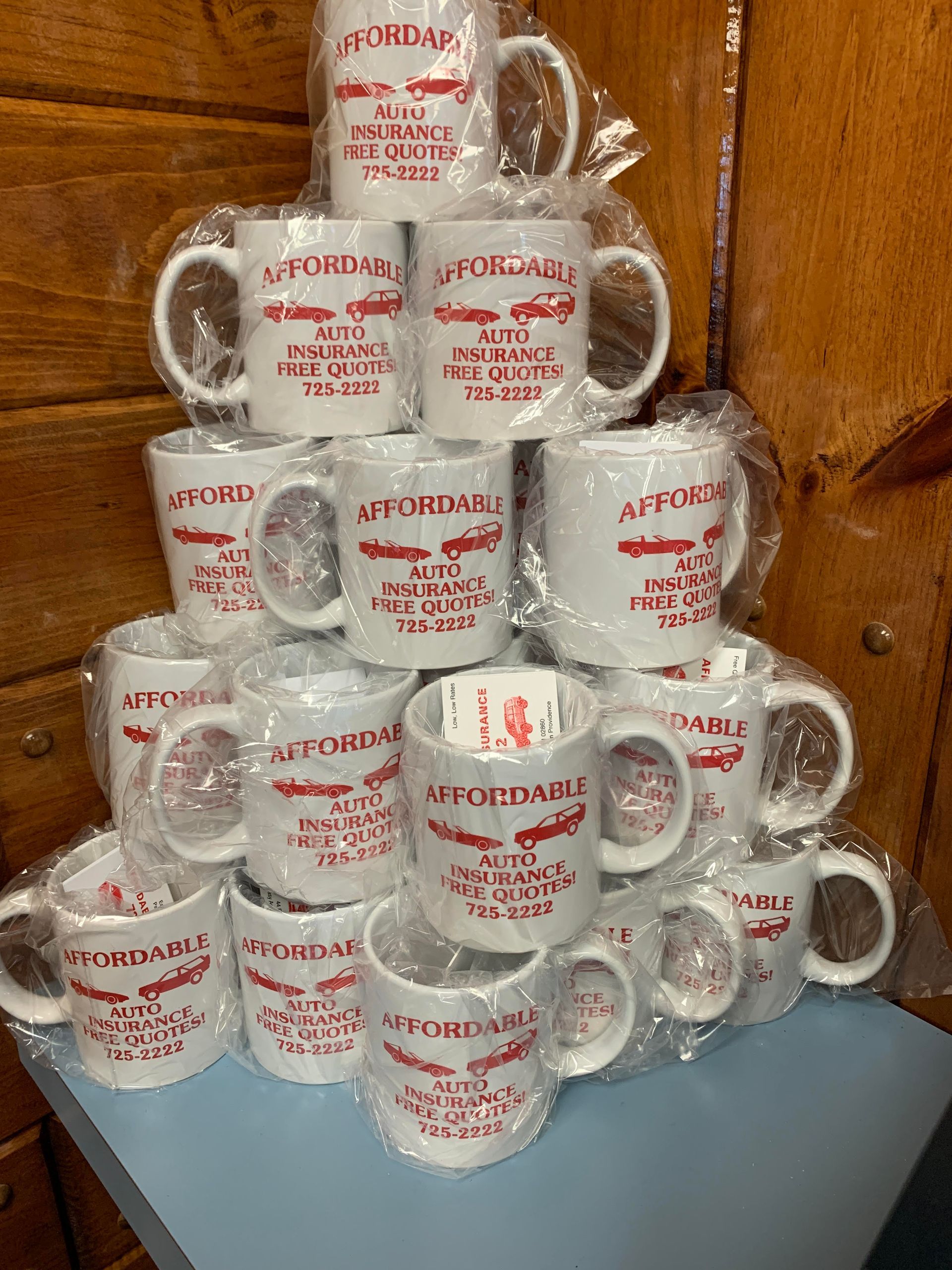 Pile of white mugs wrapped in plastic, each with red 