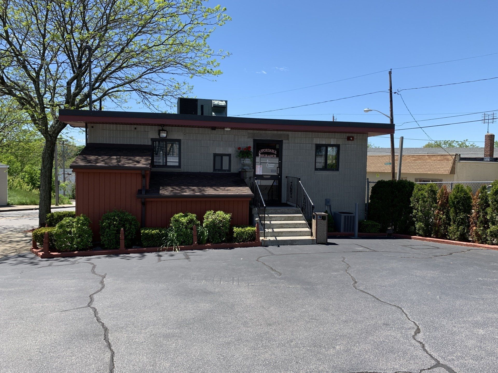A small, one-story building with an entrance, brown roof, and small bushes; sunny day.