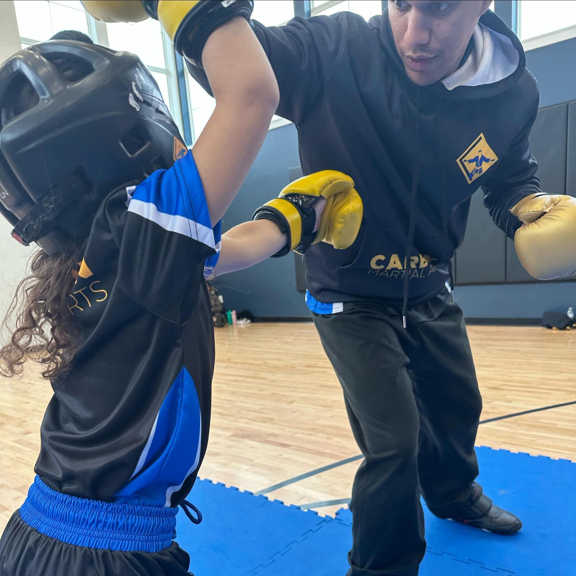 A young girl in a karate uniform is sitting on the floor.