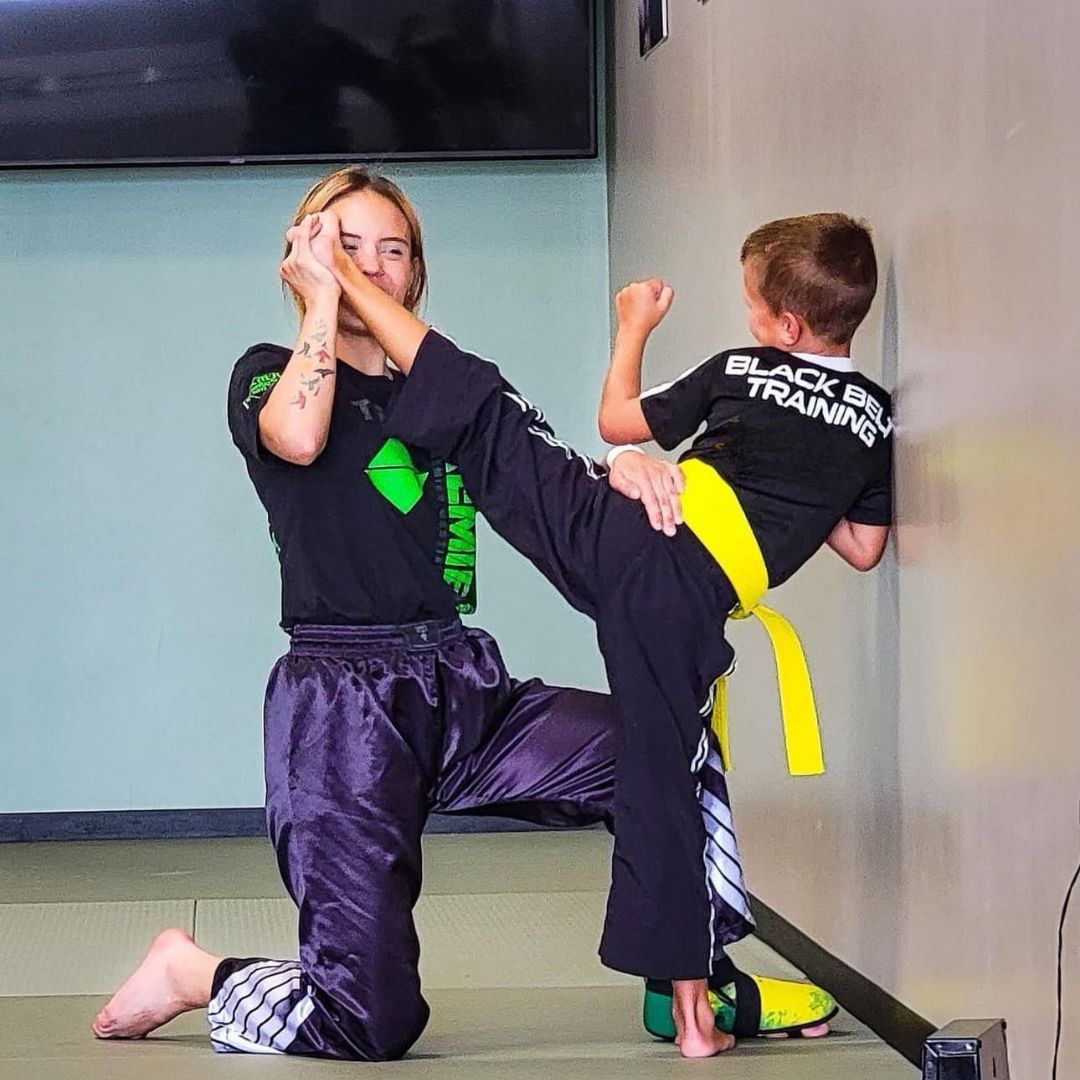 A young girl in a karate uniform is sitting on the floor.