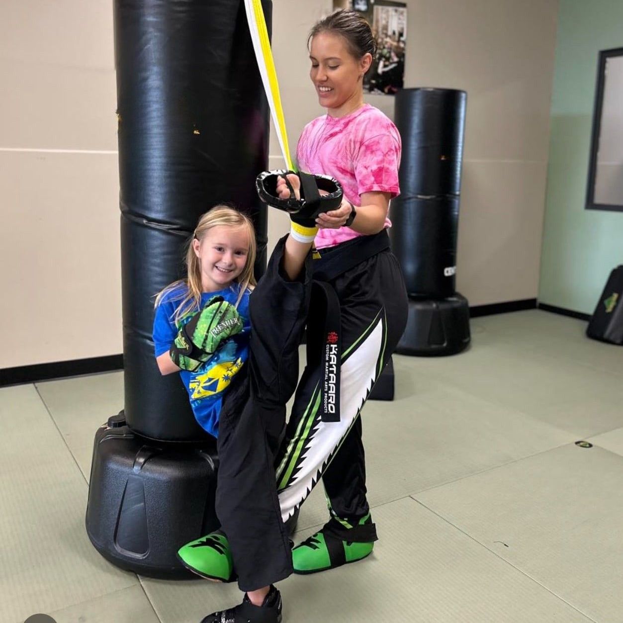 A man is kneeling down next to a young boy in a taekwondo class.