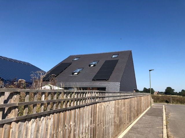 A house called Pagolin with solar panels on the roof is behind a wooden fence.