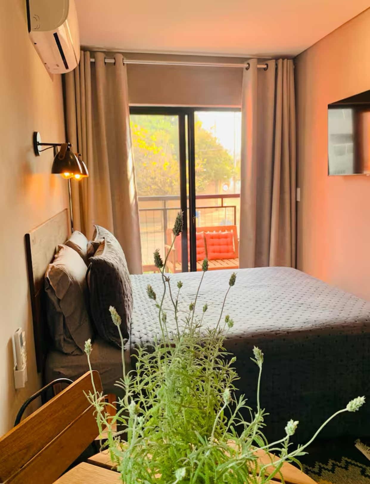 Quarto com cama, vista para a varanda, decoração em tons de cinza e bege, planta em primeiro plano.