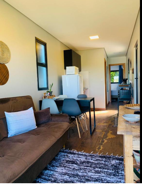 Apartamento estúdio aconchegante com sofá marrom, cozinha pequena, mesa escura e tapete.