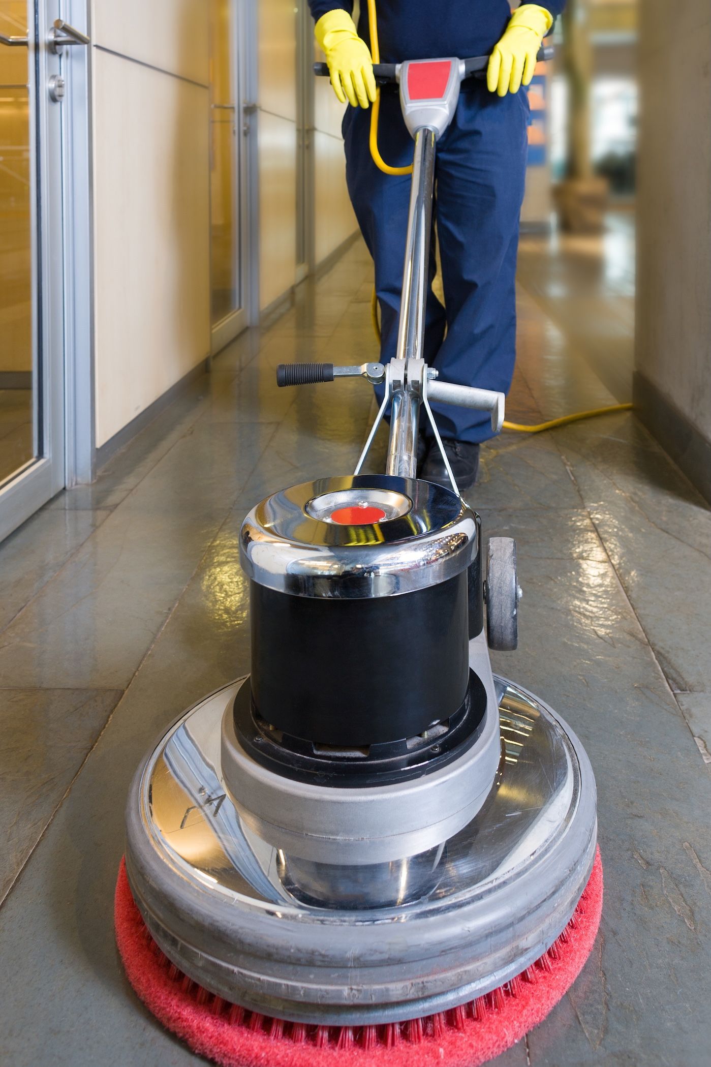 Person In Blue Pants And Yellow Gloves Using Floor Buffer In A Hallway — Rocky Commercial Cleaners In Berserker, QLD