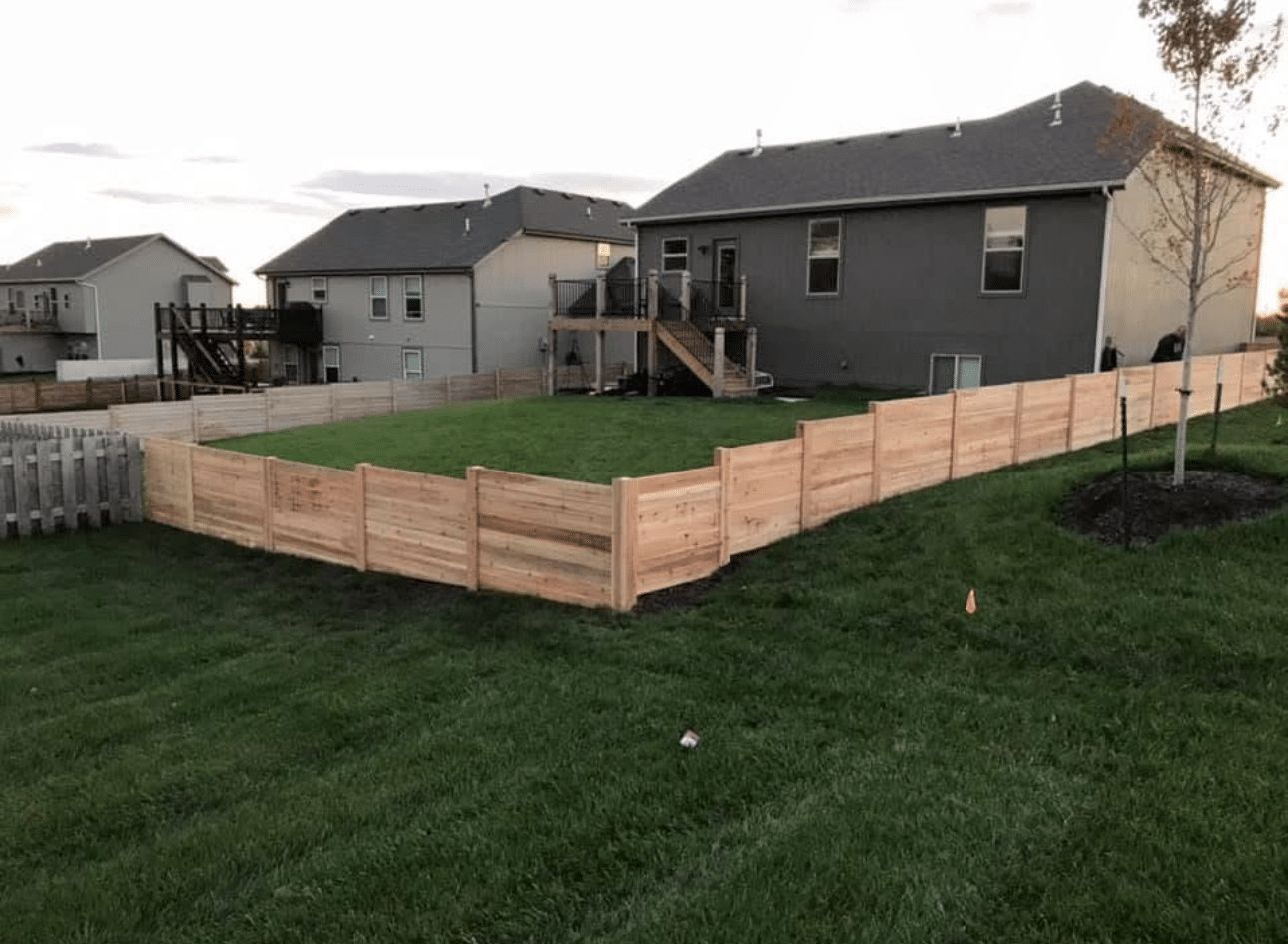 A wooden fence surrounds a lush green yard in front of a house.