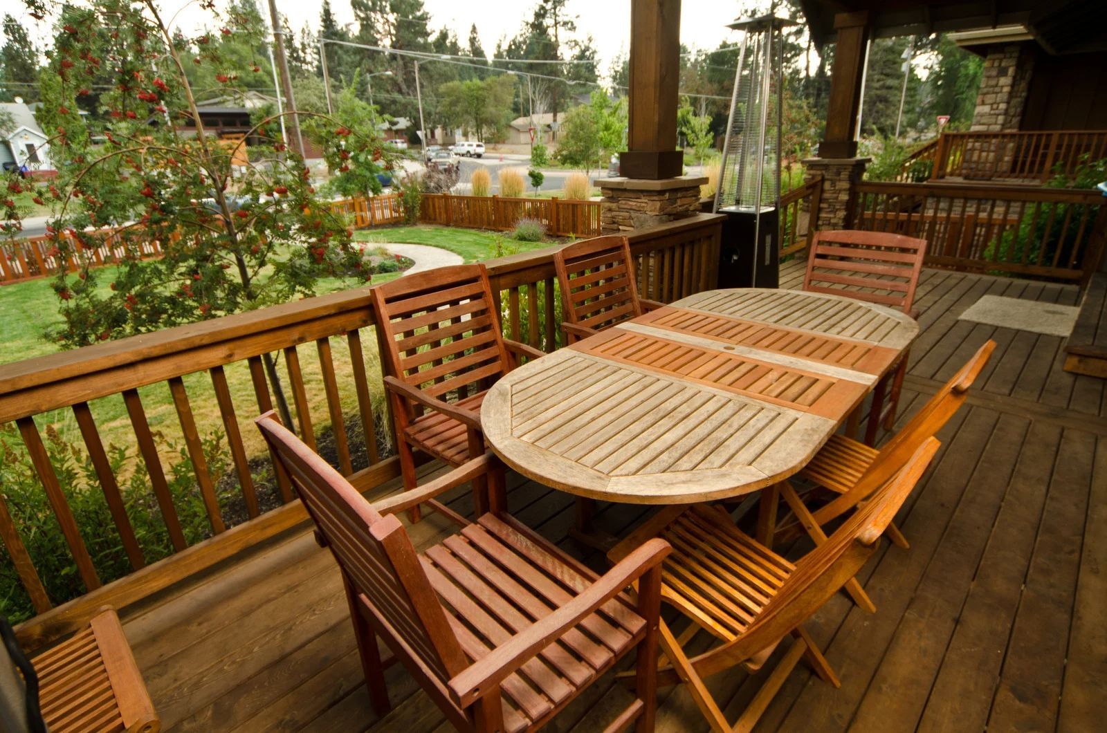 Wooden outdoor dining table with chairs on a wooden deck overlooking a lawn and trees.