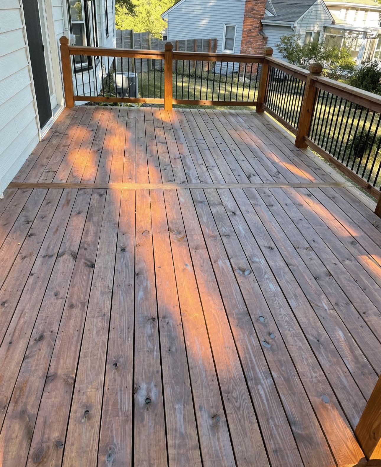 A wooden deck with a railing and a house in the background