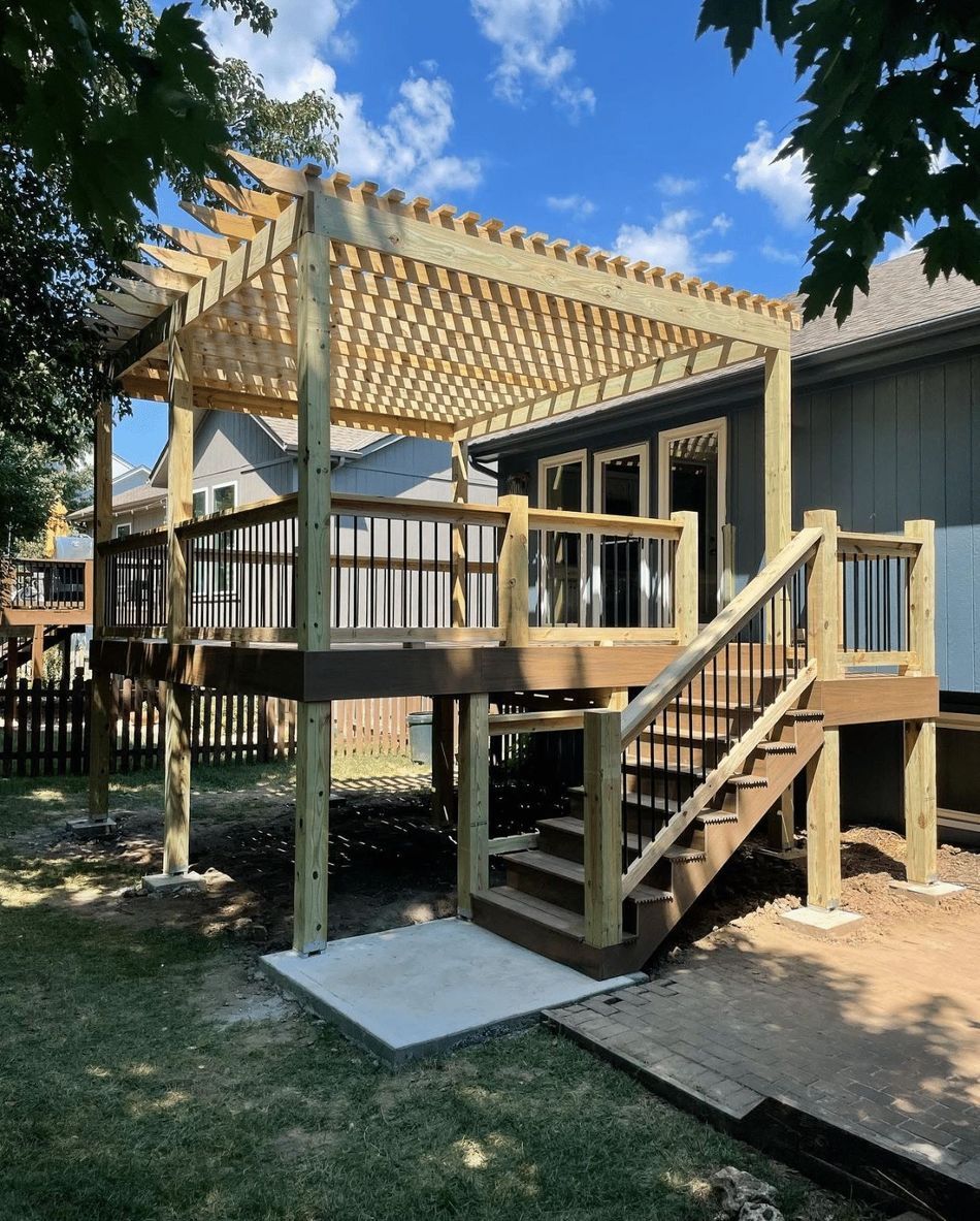 A wooden deck with stairs and a pergola in the backyard of a house.