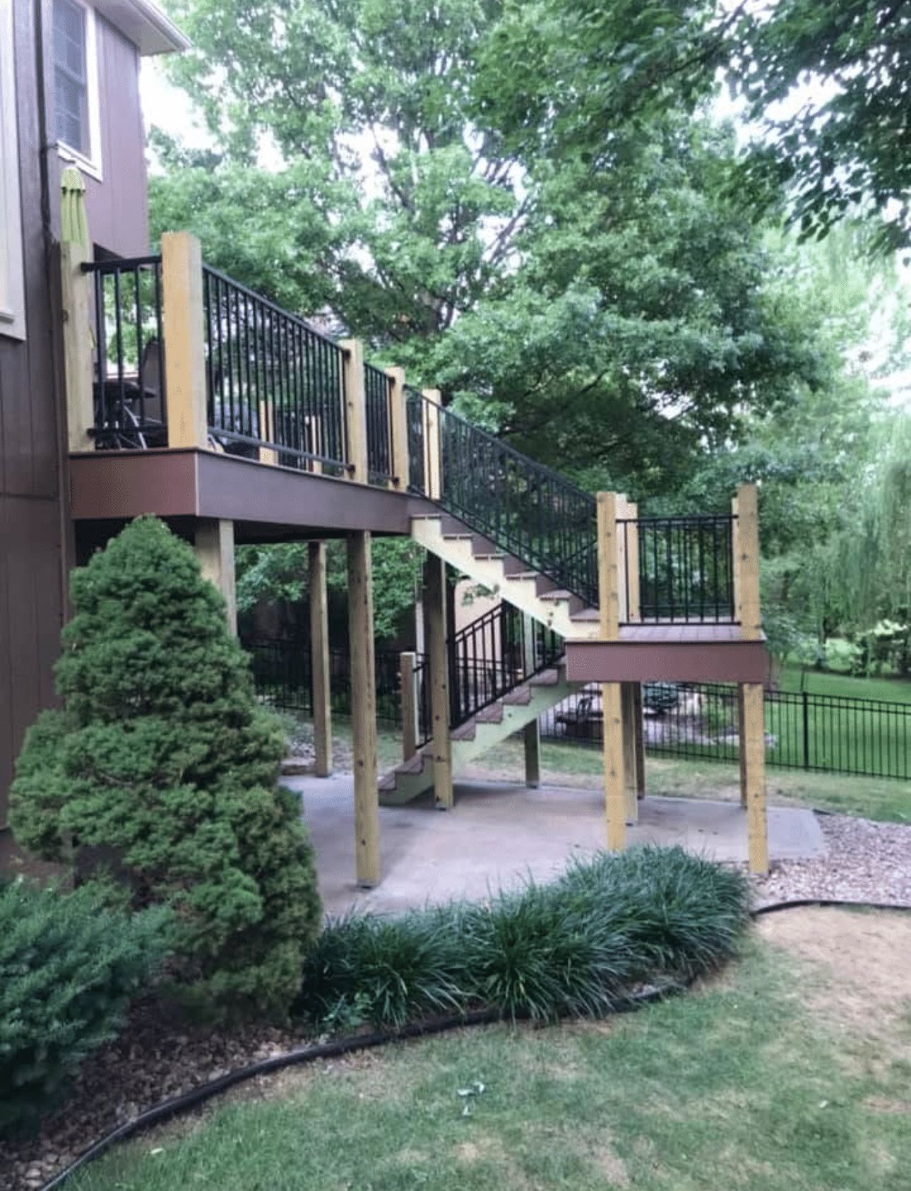 A wooden deck with stairs leading up to it is in the backyard of a house.