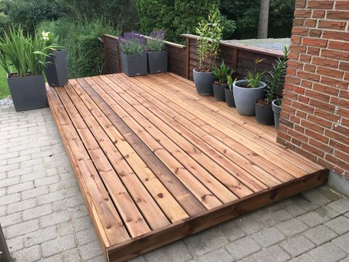 A wooden deck with potted plants on it next to a brick wall.