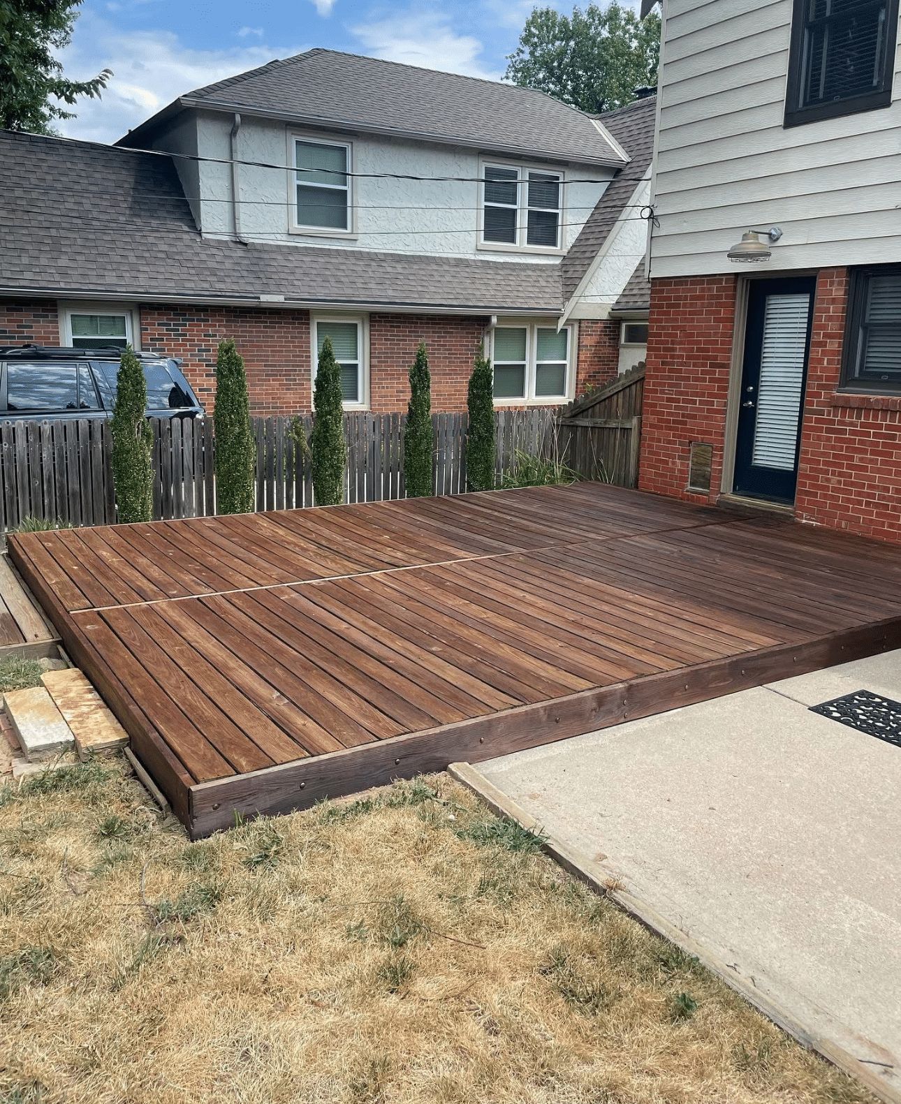 A wooden deck is in front of a brick house.