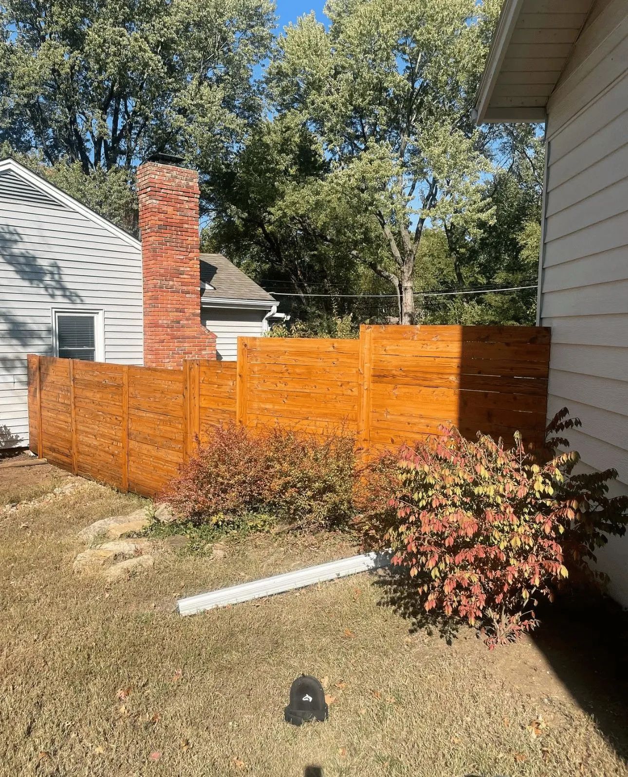 Wooden privacy fence with gate in a backyard. Green grass and cloudy sky in the background.