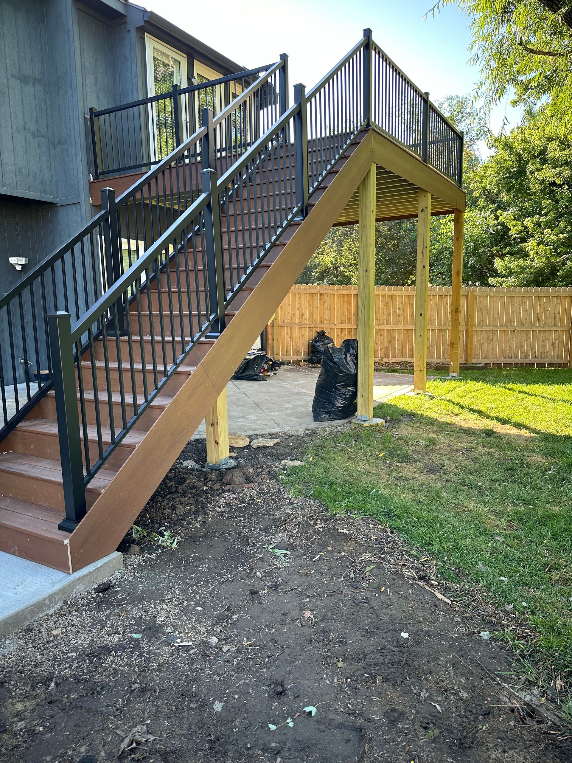Exterior view of a multi-level deck and staircase, brown and black, with a fenced backyard.