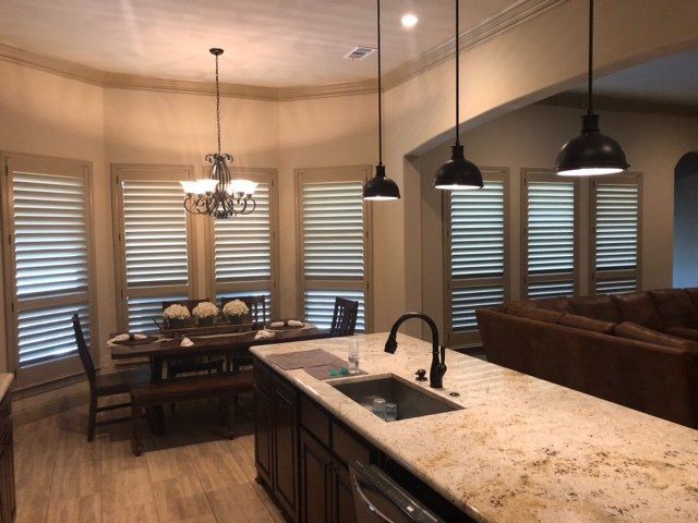 Kitchen with island, dining table, and open shuttered windows. Beige walls, granite counters, pendant lights.