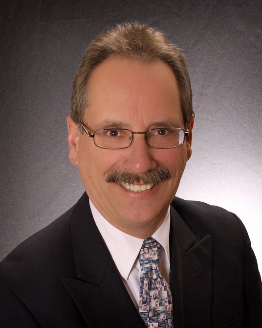 A man with glasses and a mustache is wearing a suit and tie
