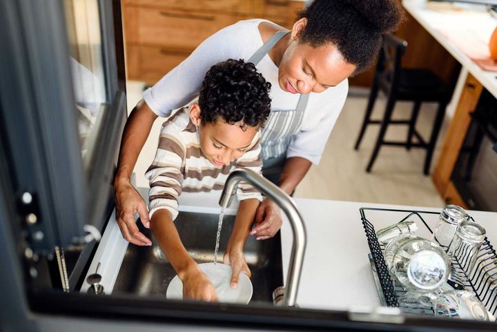 A woman and a child are washing dishes in a kitchen sink.