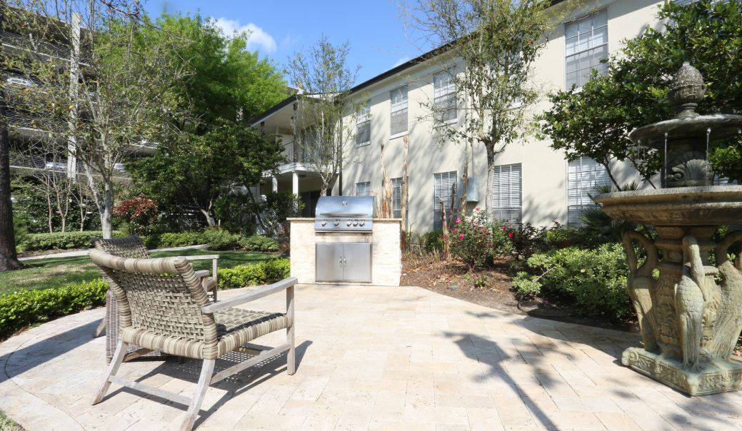 A patio with a grill and chairs in front of a building.