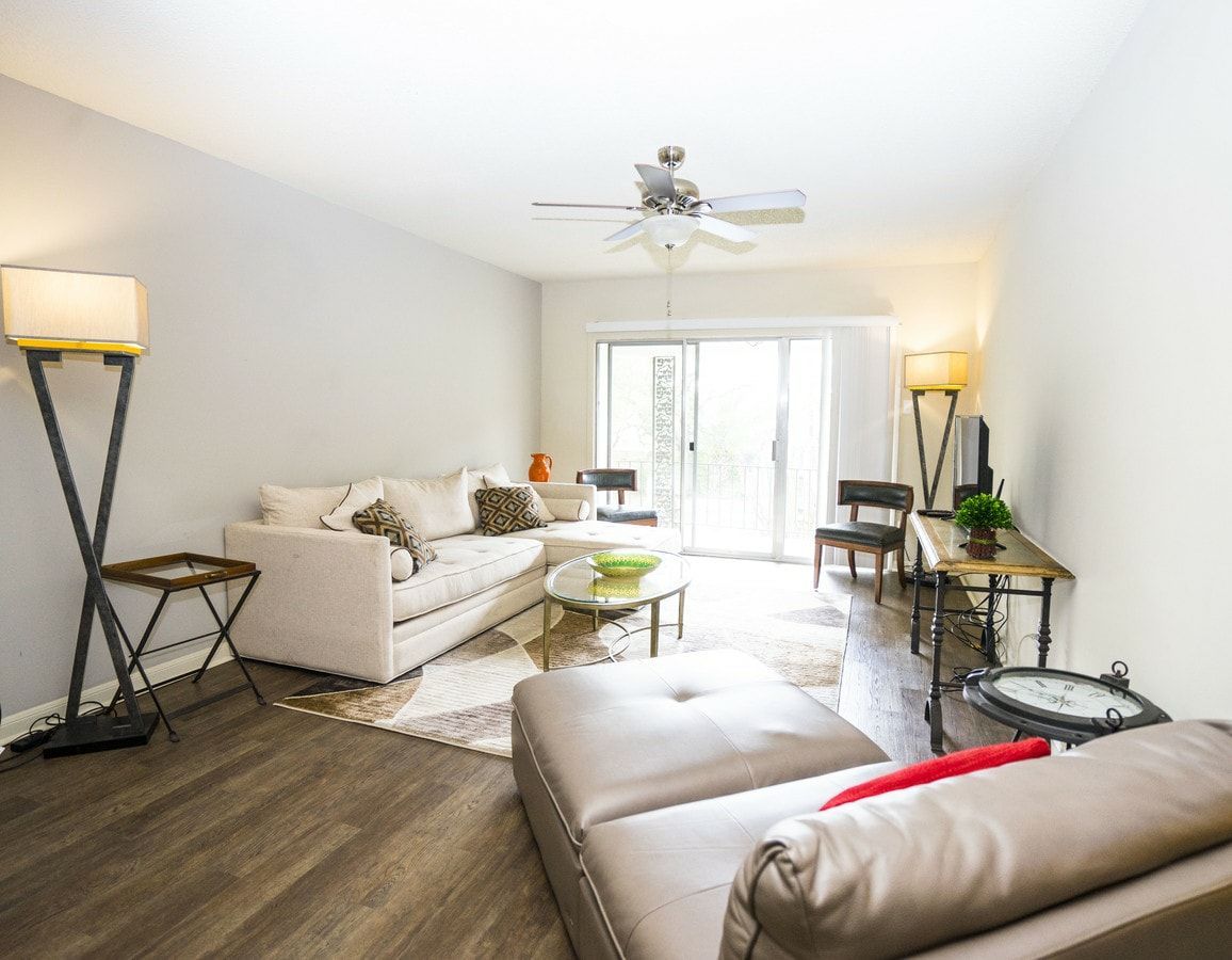 A living room with a couch , ottoman , table and ceiling fan.