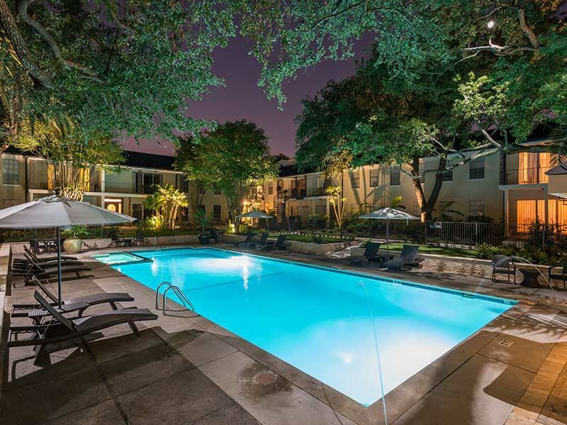 A large swimming pool is lit up at night in front of a building.