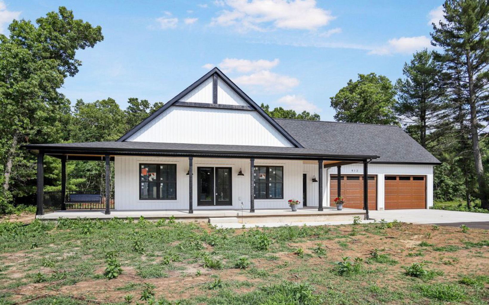 White farmhouse with black trim and brown garage doors.