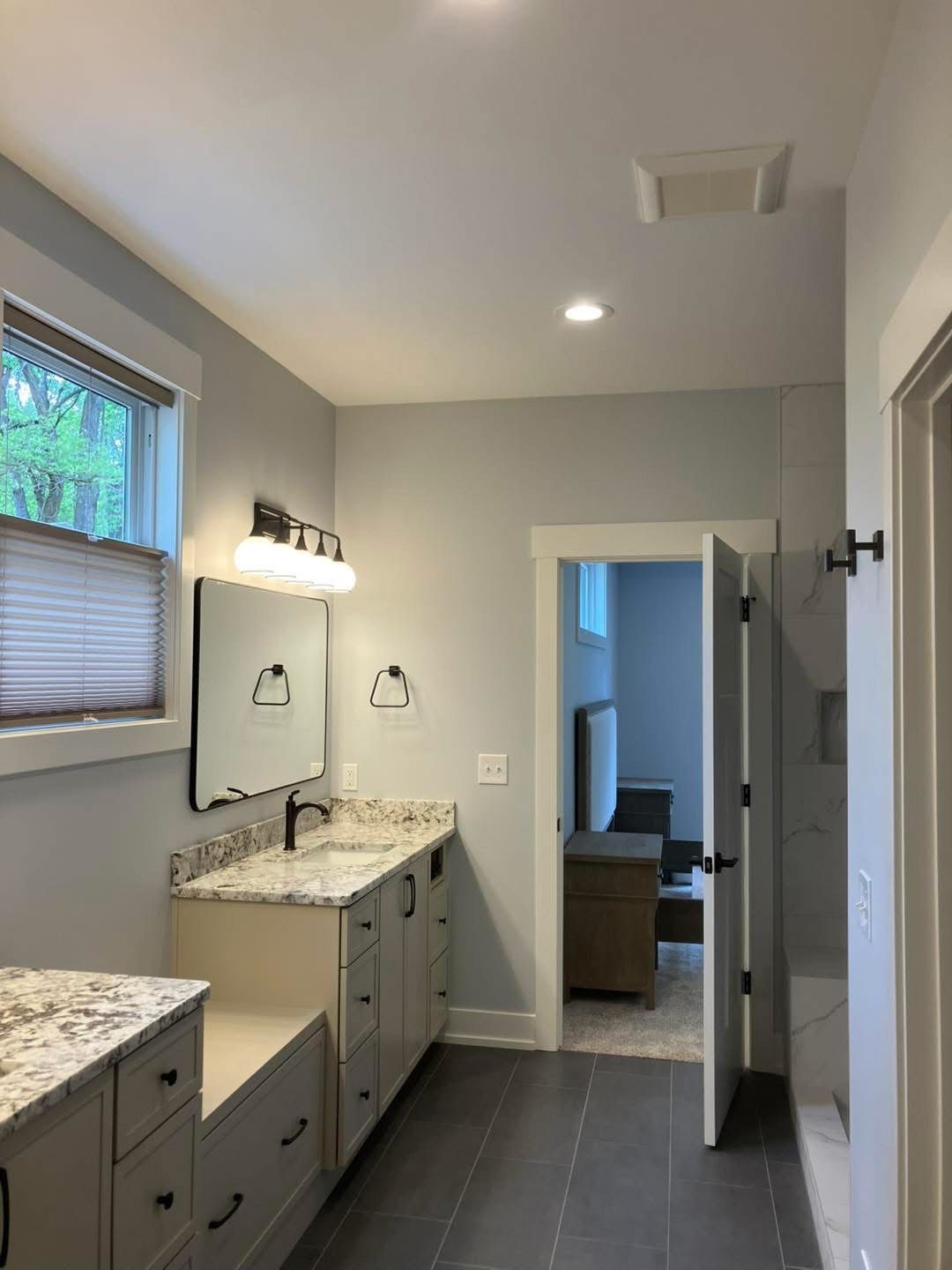 Bathroom with gray walls, vanity, dark countertops, and a door leading to another room.