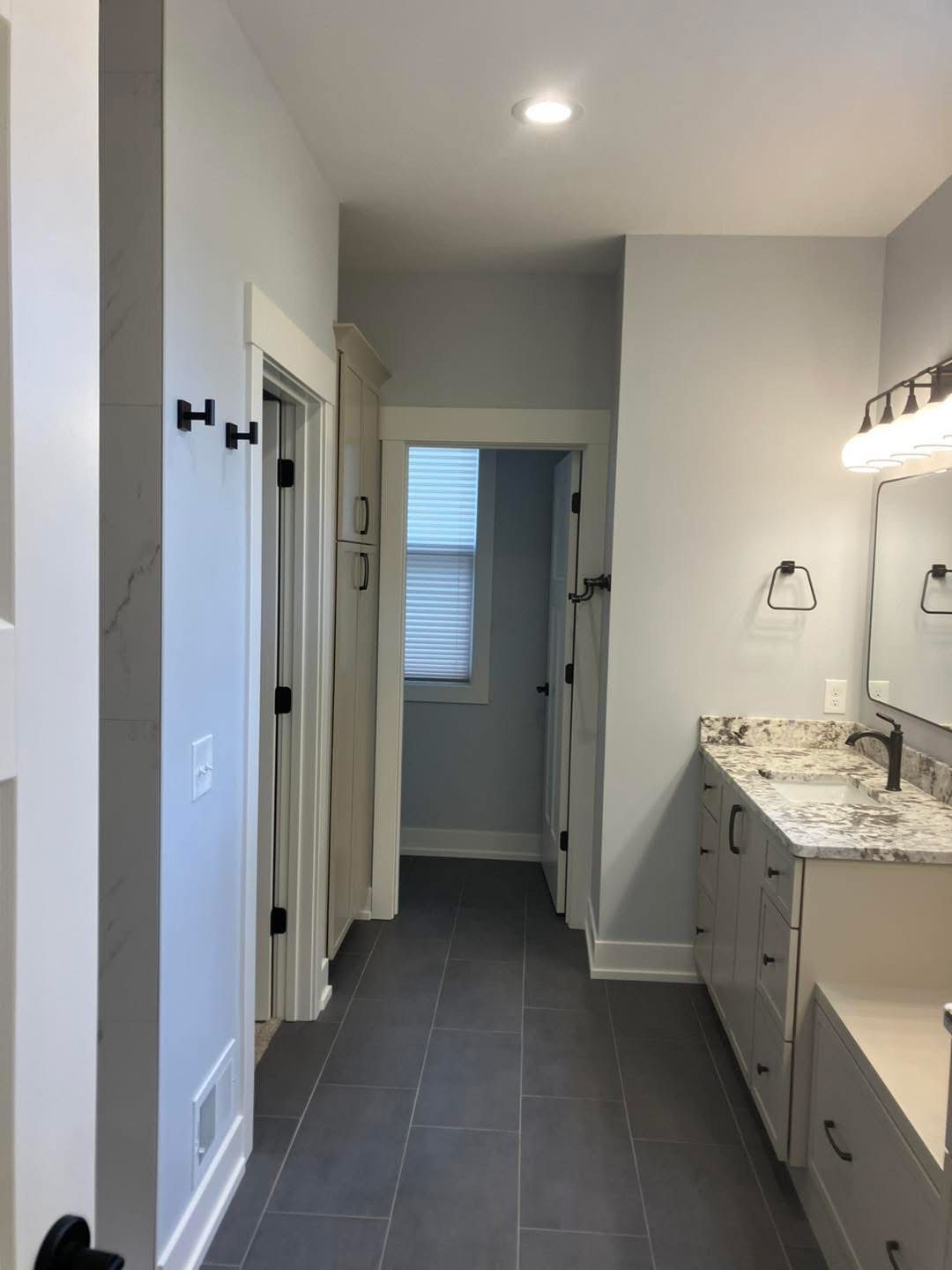 Bathroom hallway with gray tile floor, white cabinets, and light gray walls.