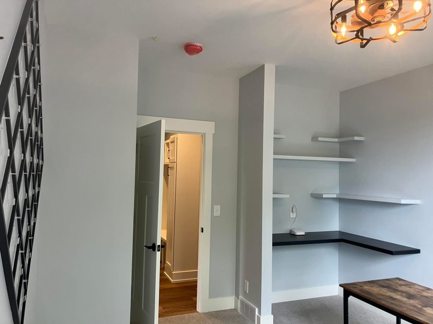 A light grey bedroom with a desk, shelves, and a closet.