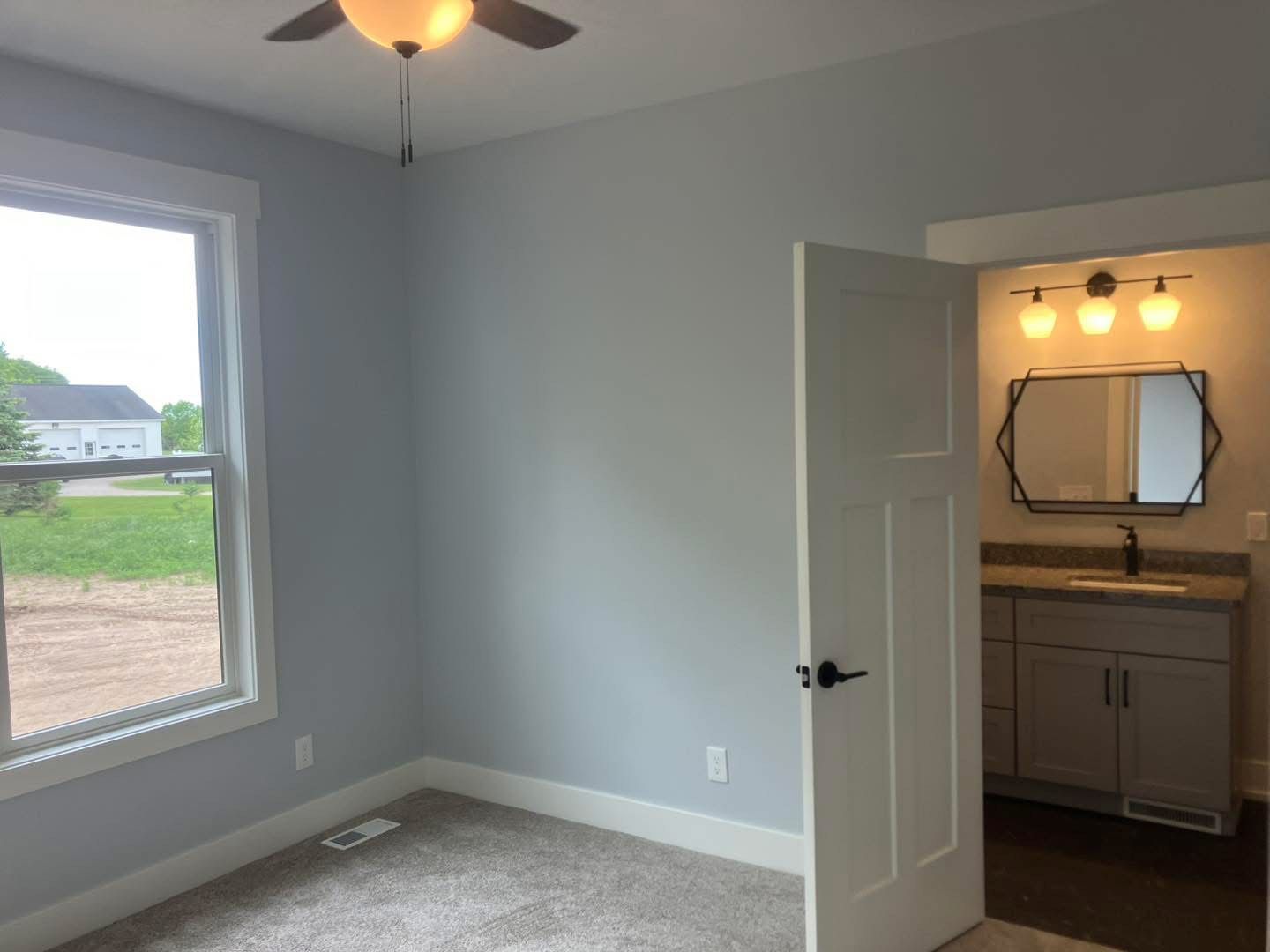 Bedroom with gray walls, window, door to bathroom with vanity and mirror.