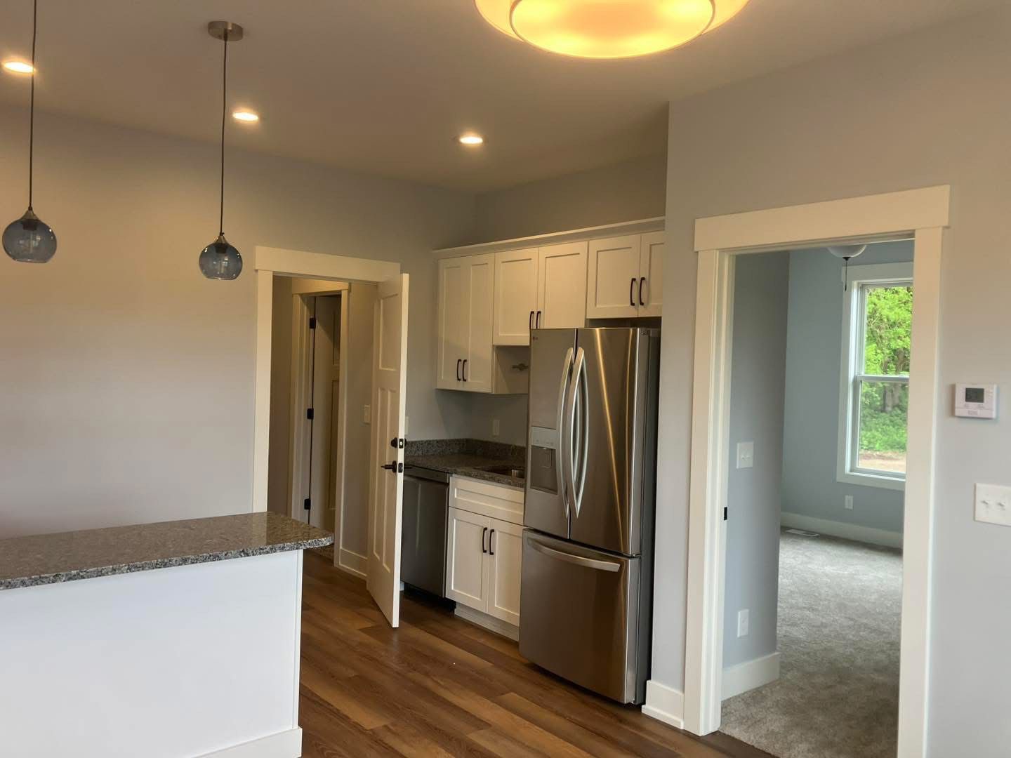 Kitchen with white cabinets, stainless steel appliances, granite counters, and a doorway to another room.