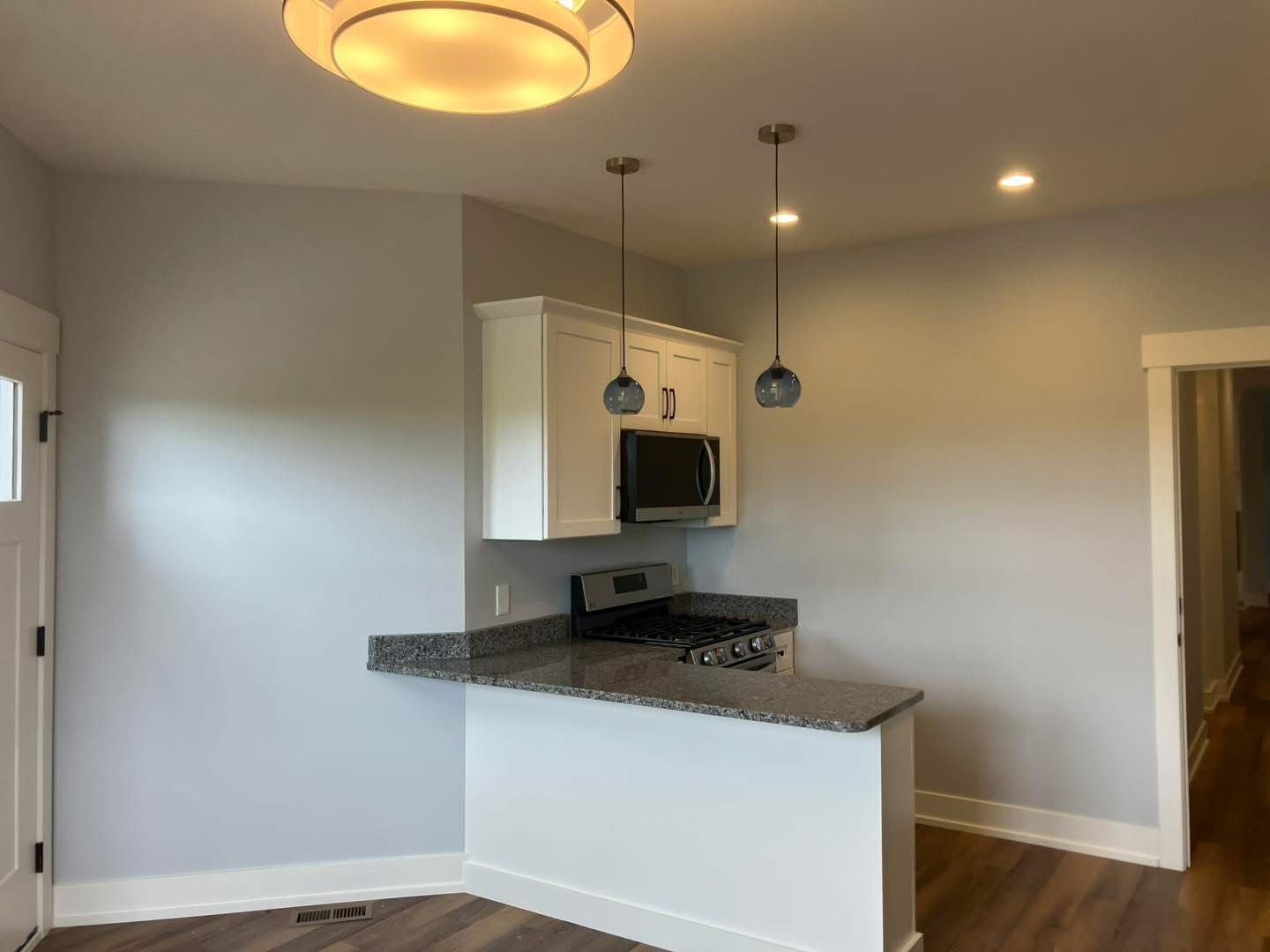 Small kitchen with white cabinets, gray countertops, and two pendant lights.