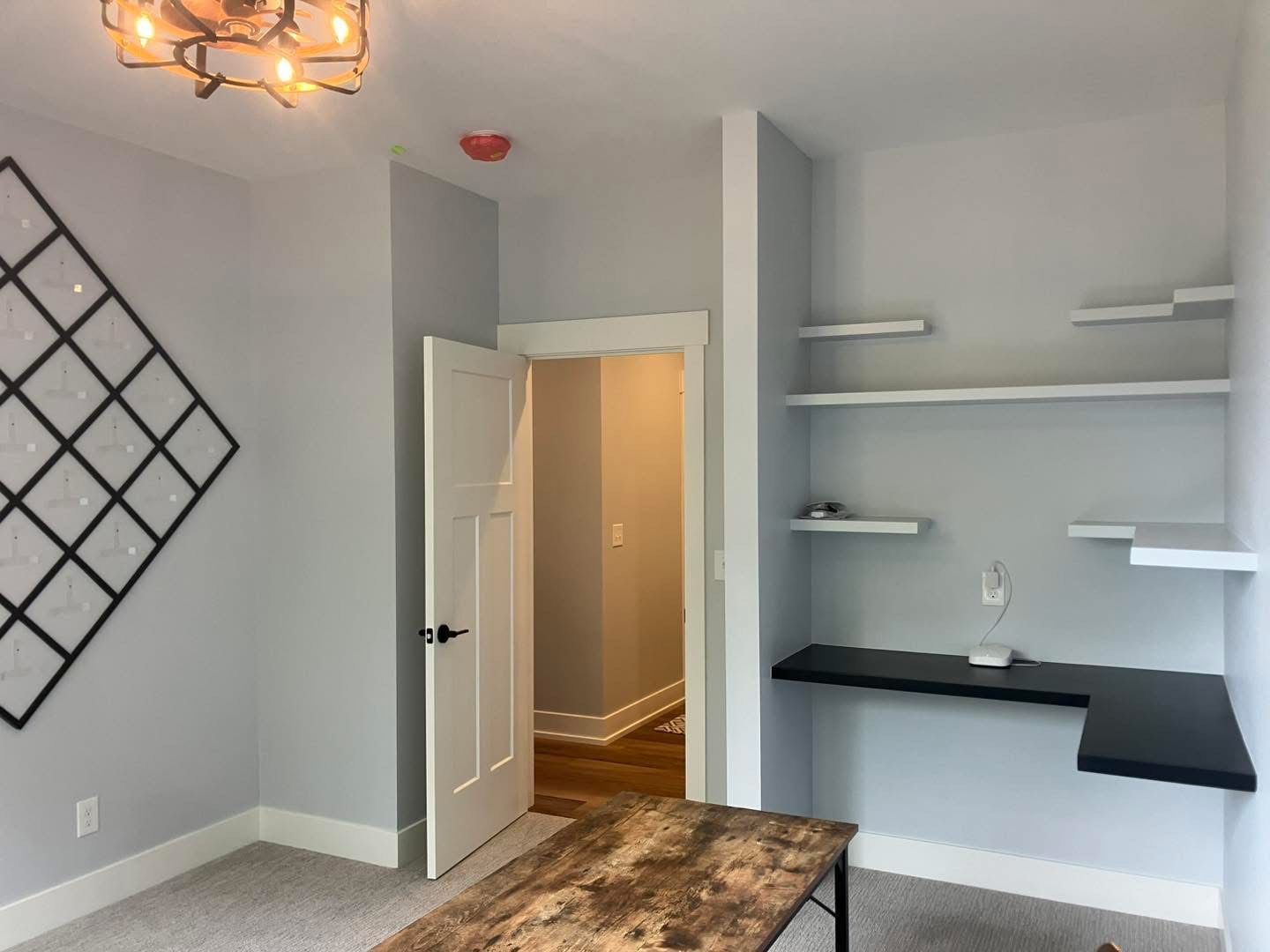 A light gray office with a desk, shelves, and open door to a hallway.