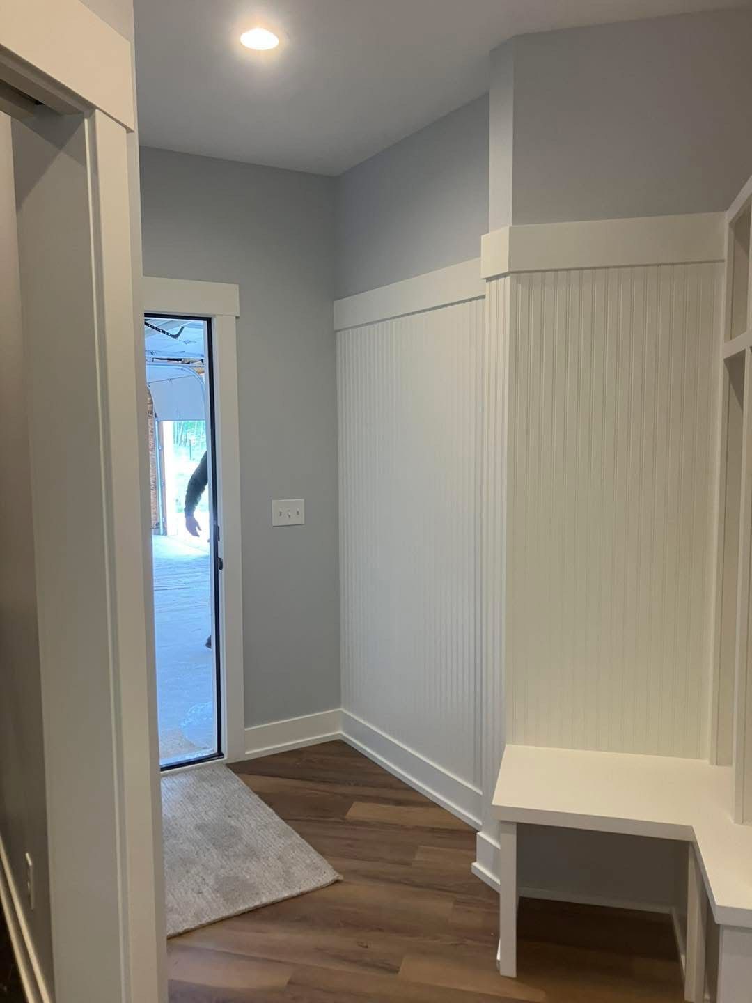 Entryway with light blue walls, white trim, and wood-look flooring. Includes a bench and door leading outside.