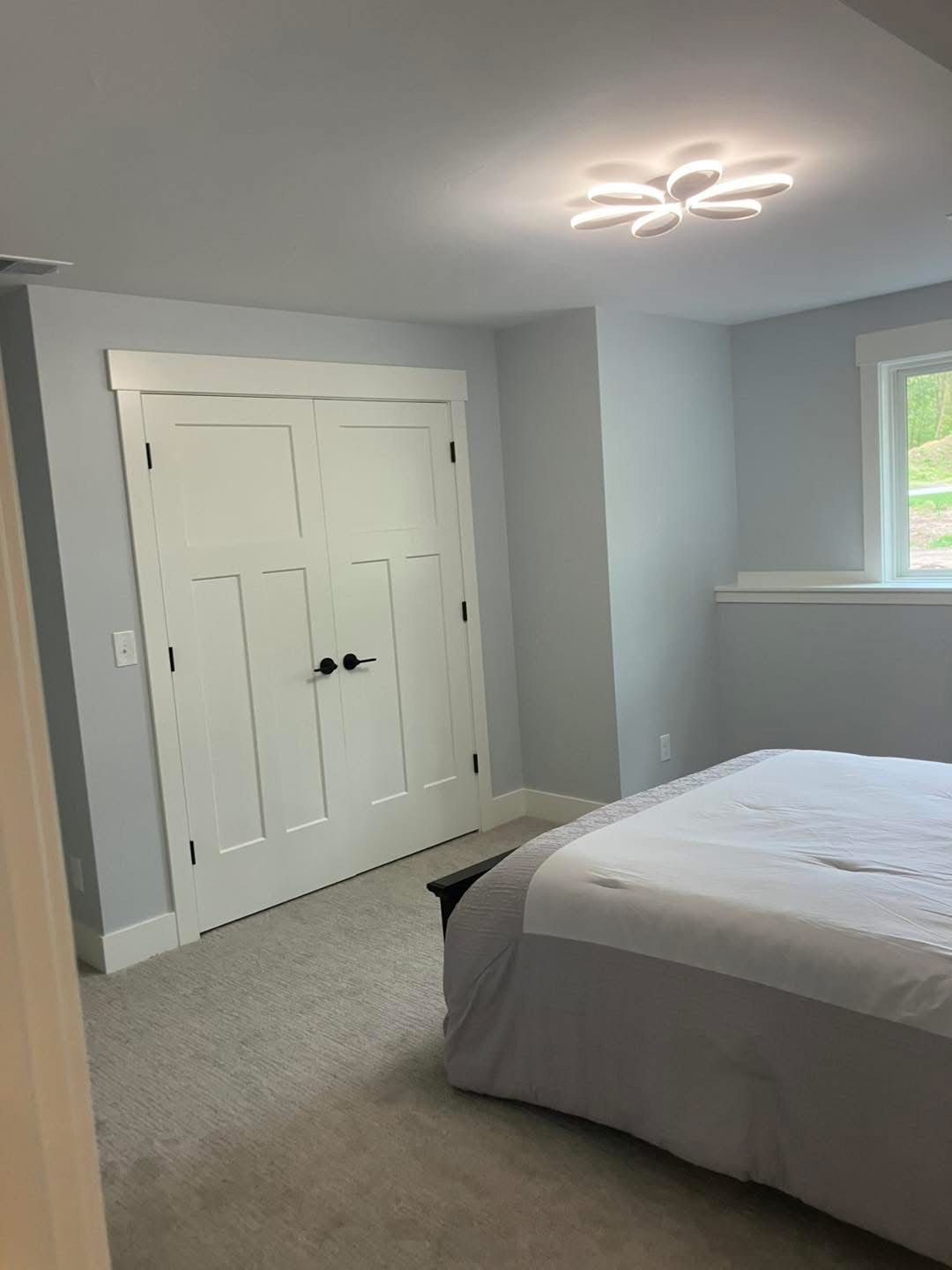 Bedroom with white closet doors, light blue walls, gray carpet, and bed with gray bedding.