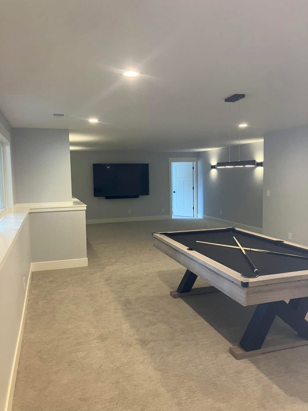 Basement game room with a pool table, large TV, and neutral-toned walls and carpet.