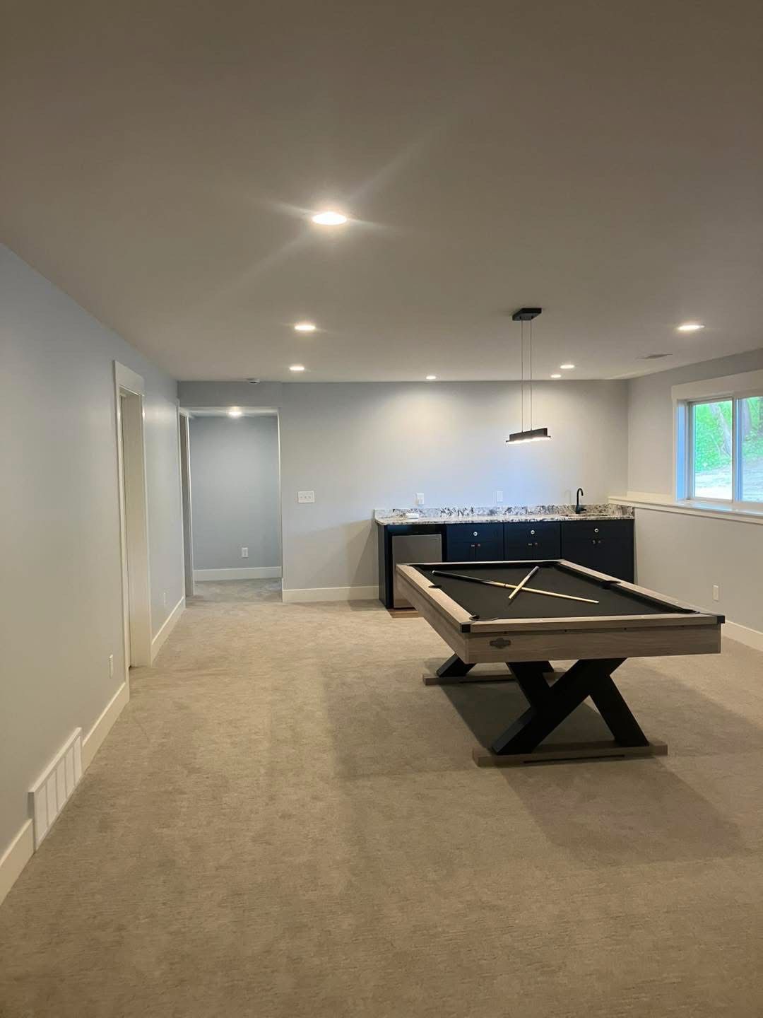 A finished basement with a pool table, bar area, and light gray walls.