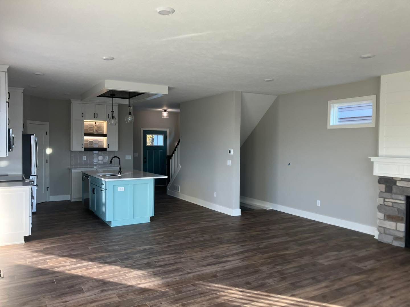 Spacious open-concept kitchen and living area with wood-look floors. Light blue island and fireplace.