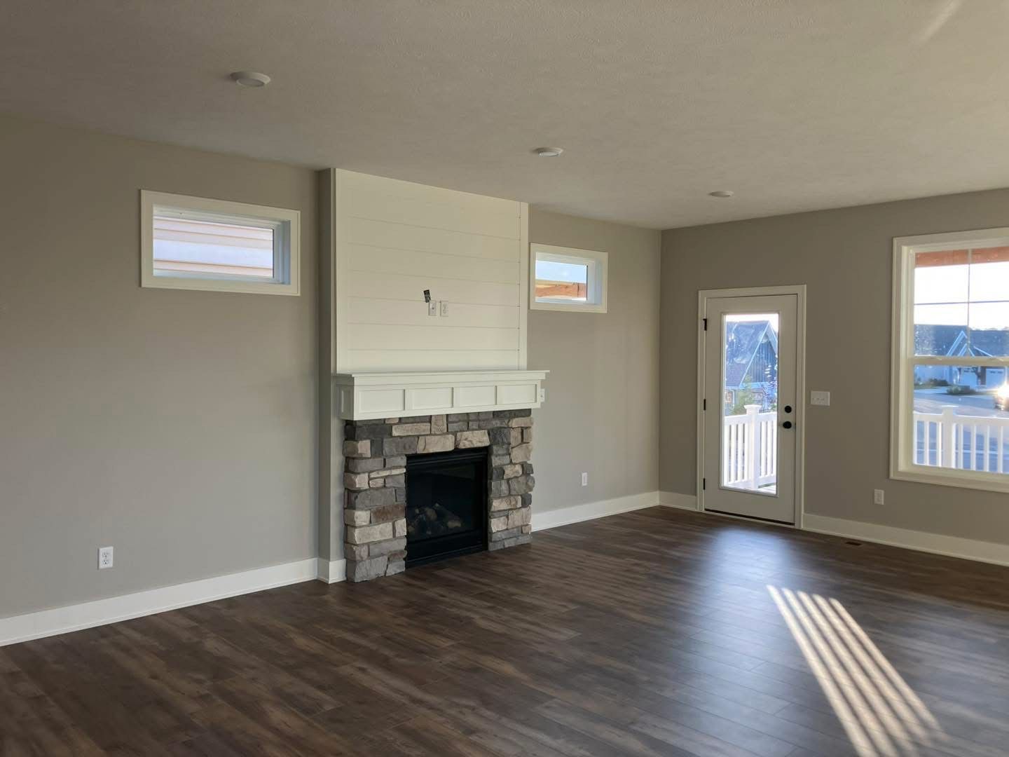 Empty living room with fireplace, windows, and a door, with wooden floors and neutral paint.