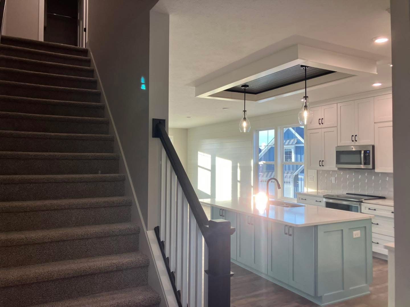 Staircase with carpeted steps next to a kitchen with a light blue island and white cabinets.