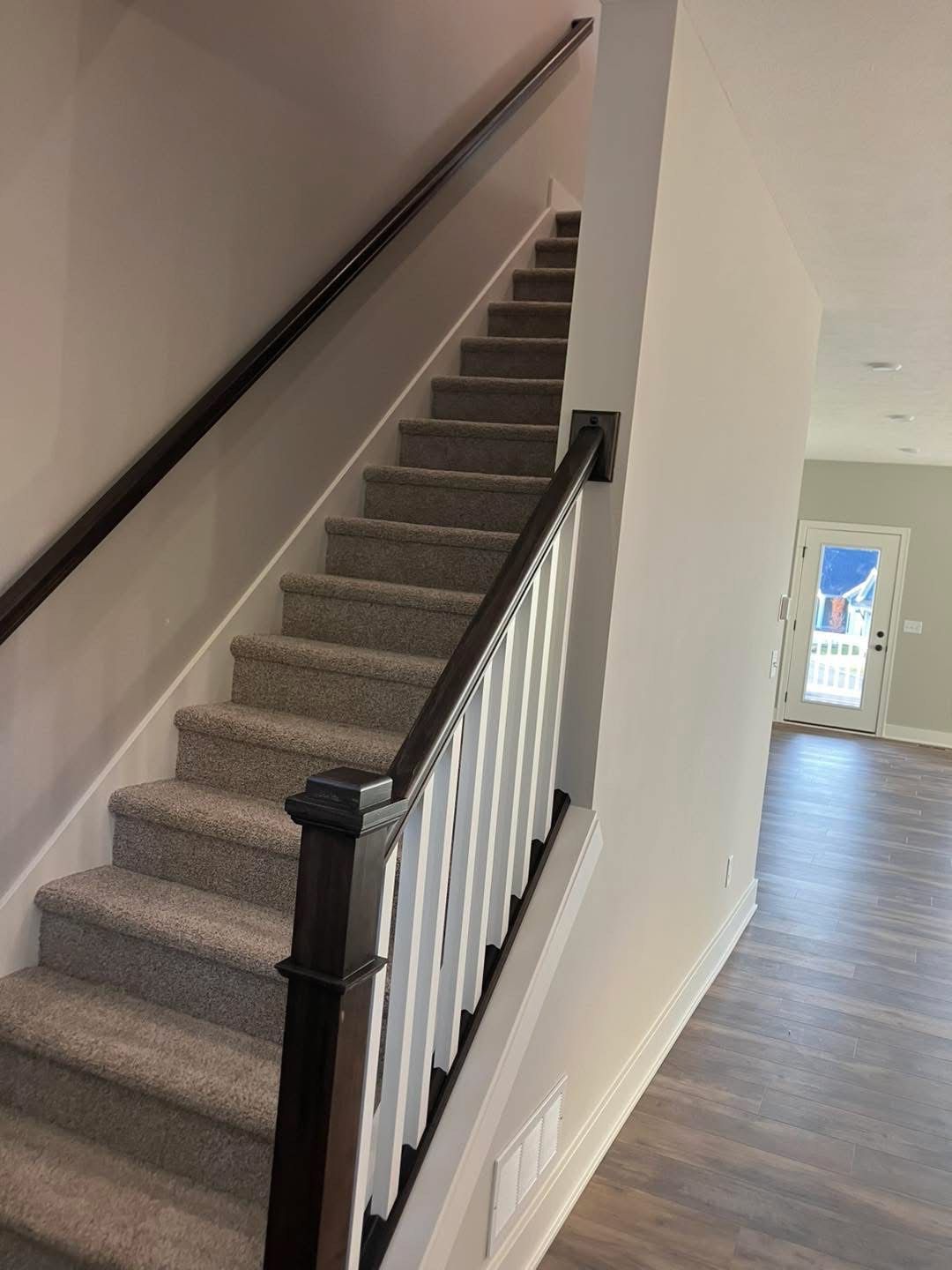 Staircase with carpeted steps, dark wood handrails and white vertical balusters, in a home.