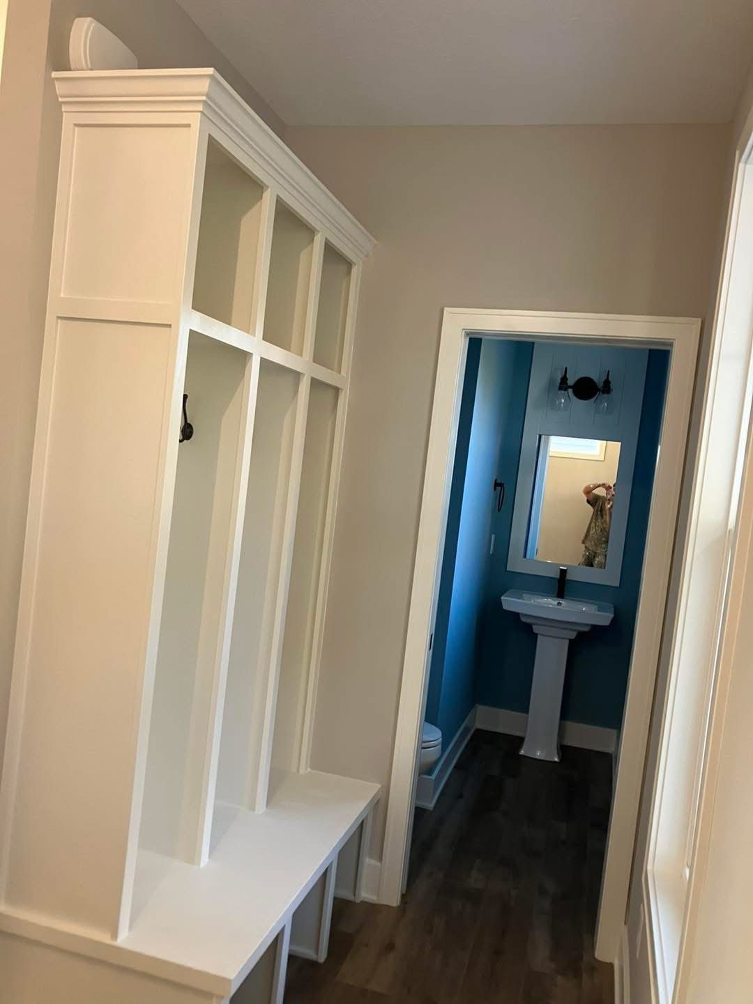 White built-in storage unit with bench in hallway, doorway to small bathroom with blue walls.
